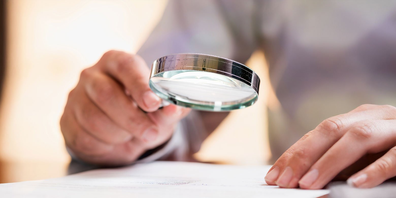 Person inspecting papers with a magnifying glass