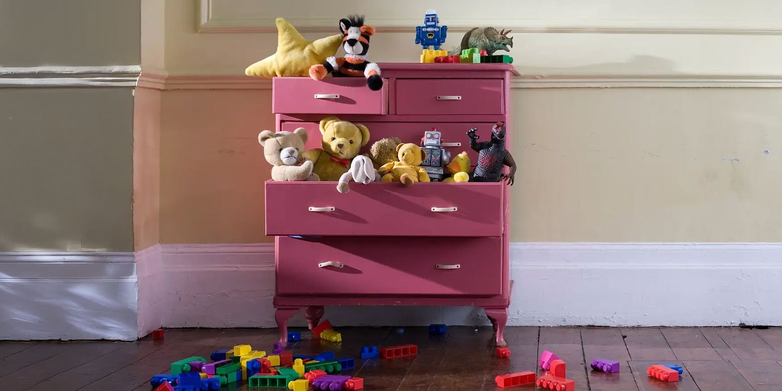 A pink dresser with stuffed animals in one drawer and building blocks on the floor