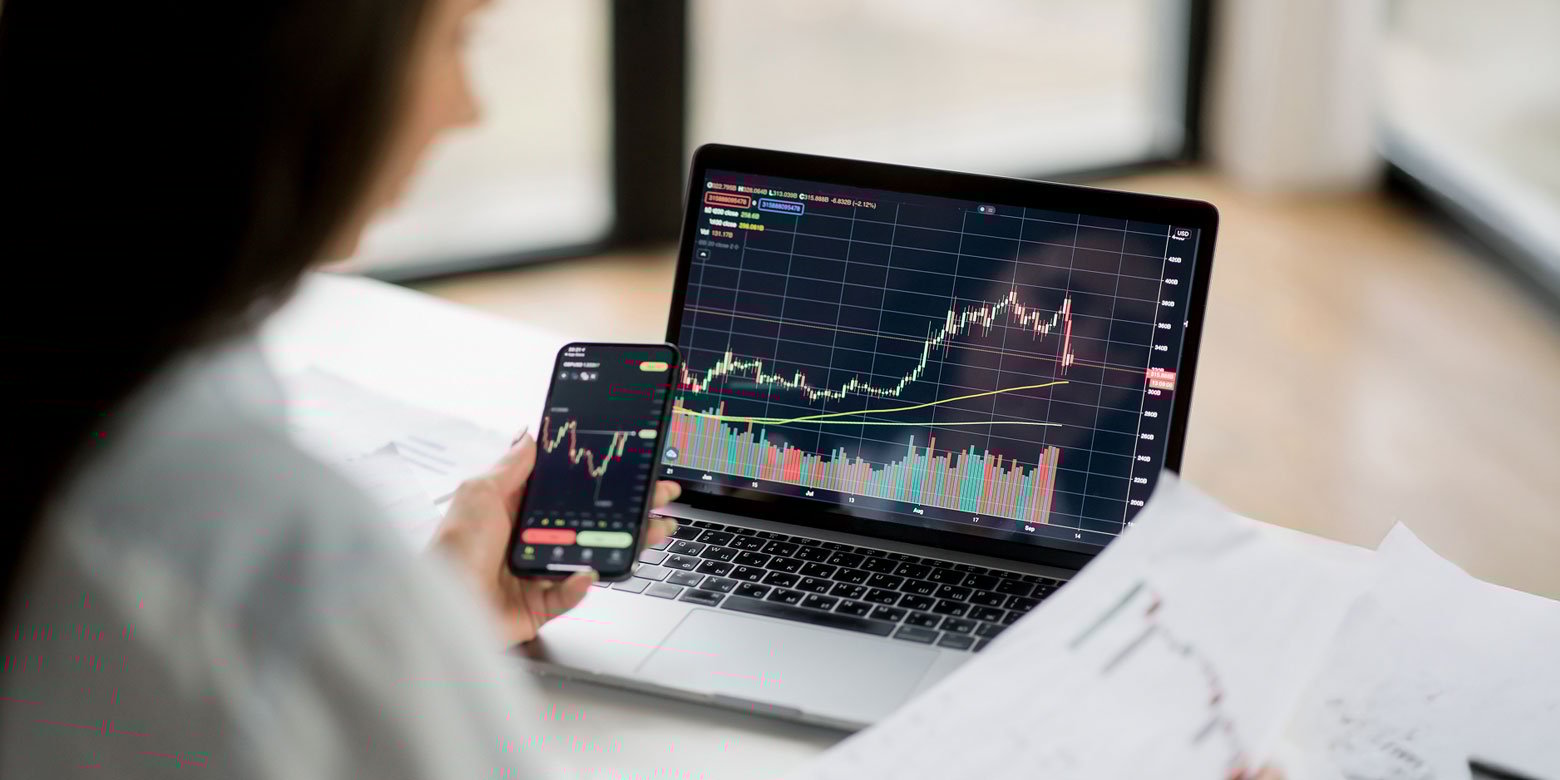 Woman comparing stock charts from a phone and laptop