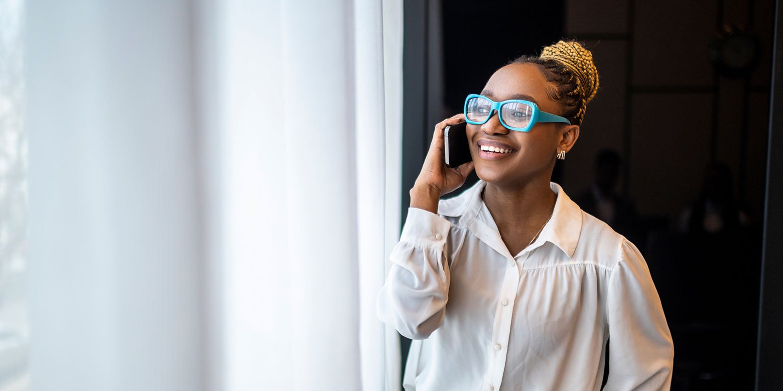 Woman in glasses smiling and talking on her cell phone to her financial planner about a fund's alpha.
