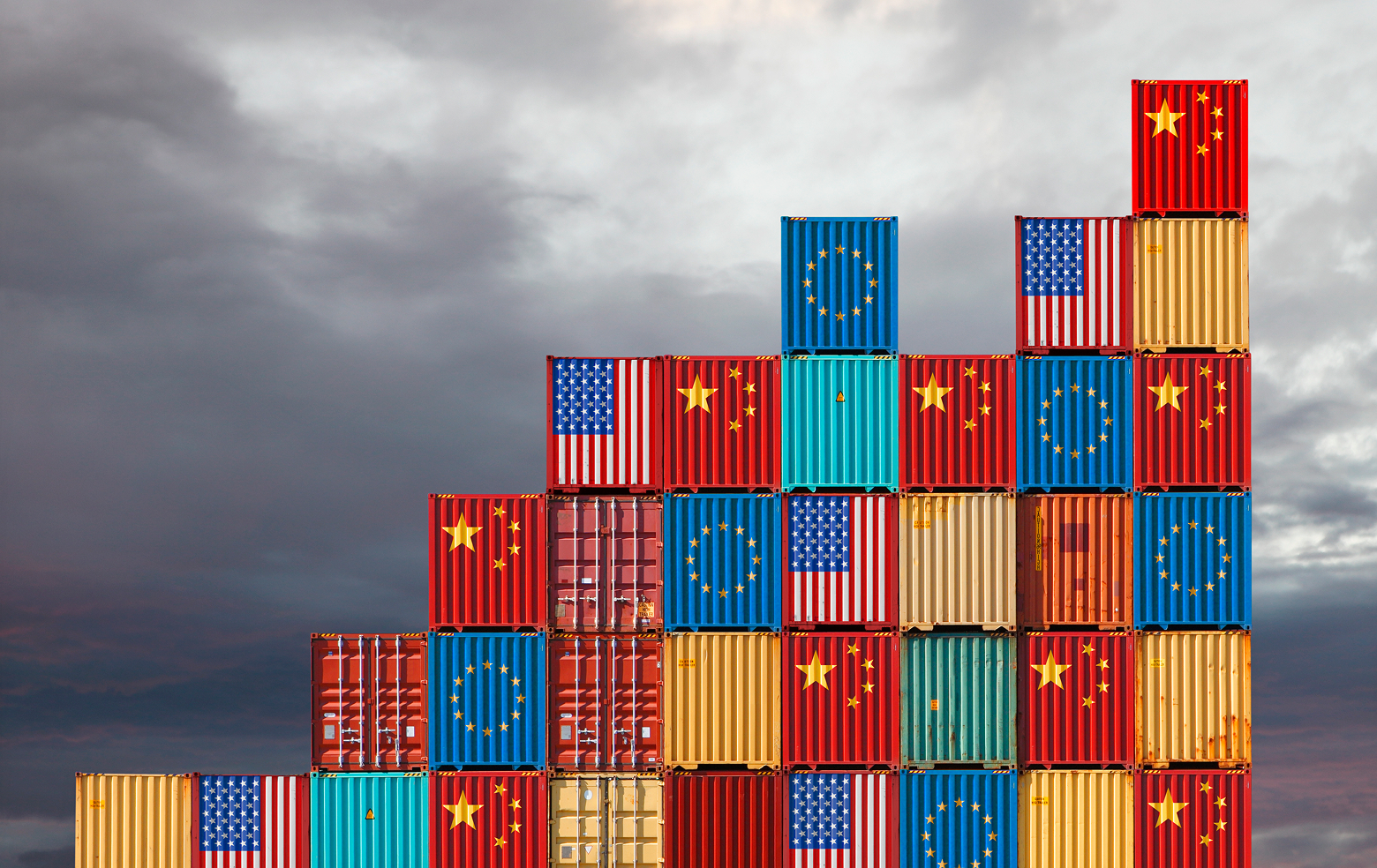 Shipping containers painted the colors of different flags are stacked on top of one another against an ominous grey sky.